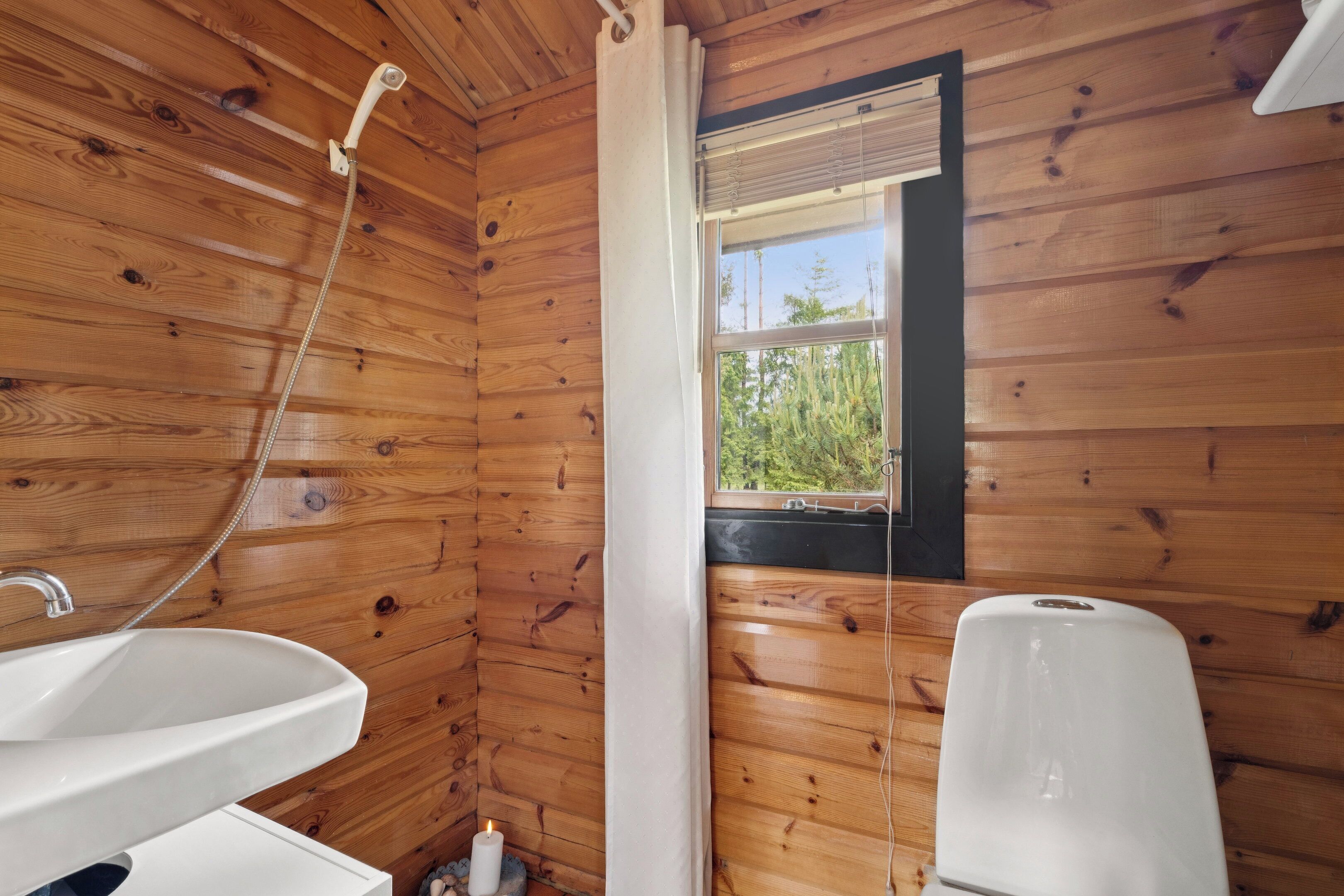 Une salle de bain rustique, située dans une cabane en bois, et équipée d’un lavabo, d’une douche et d’une fenêtre.