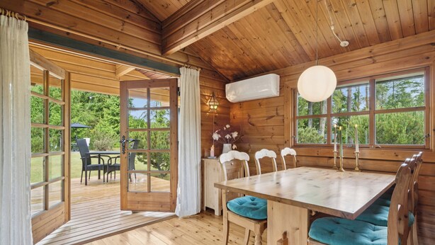 Un intérieur en bois avec une table à manger, des chaises et une vue dégagée grâce à de grandes fenêtres.