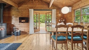 L’intérieur d’un chalet en bois, avec une cheminée, une table à manger, des chaises et de grandes fenêtres.