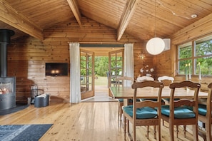 A wooden cabin interior with a fireplace, dining table, chairs, and large windows.