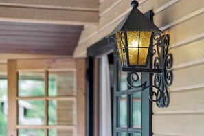 A wall-mounted lantern with a geometric glass pattern, attached to a building with wooden siding and a window with multiple panes.