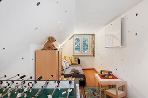 Lastenhuone, jossa on sänky, pieni pöytä, jossa on leluja, pöytäjalkapallopeli ja ikkuna, jossa on verhot.