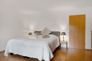 Ein Schlafzimmer mit einem Bett, zwei Nachttischlampen, einem Nachttisch und einer Holztür.