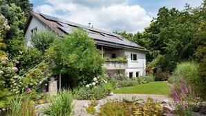 Une maison à deux étages avec un jardin, un étang et des panneaux solaires sur le toit.