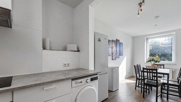 Una cocina moderna con lavavajillas, lavadora integrada y comedor con mesa y sillas.