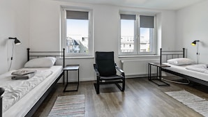 Un dormitorio con dos camas, una silla, una mesa y dos ventanas.
