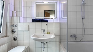 Un baño con lavamanos, espejo, inodoro y ducha blancos.