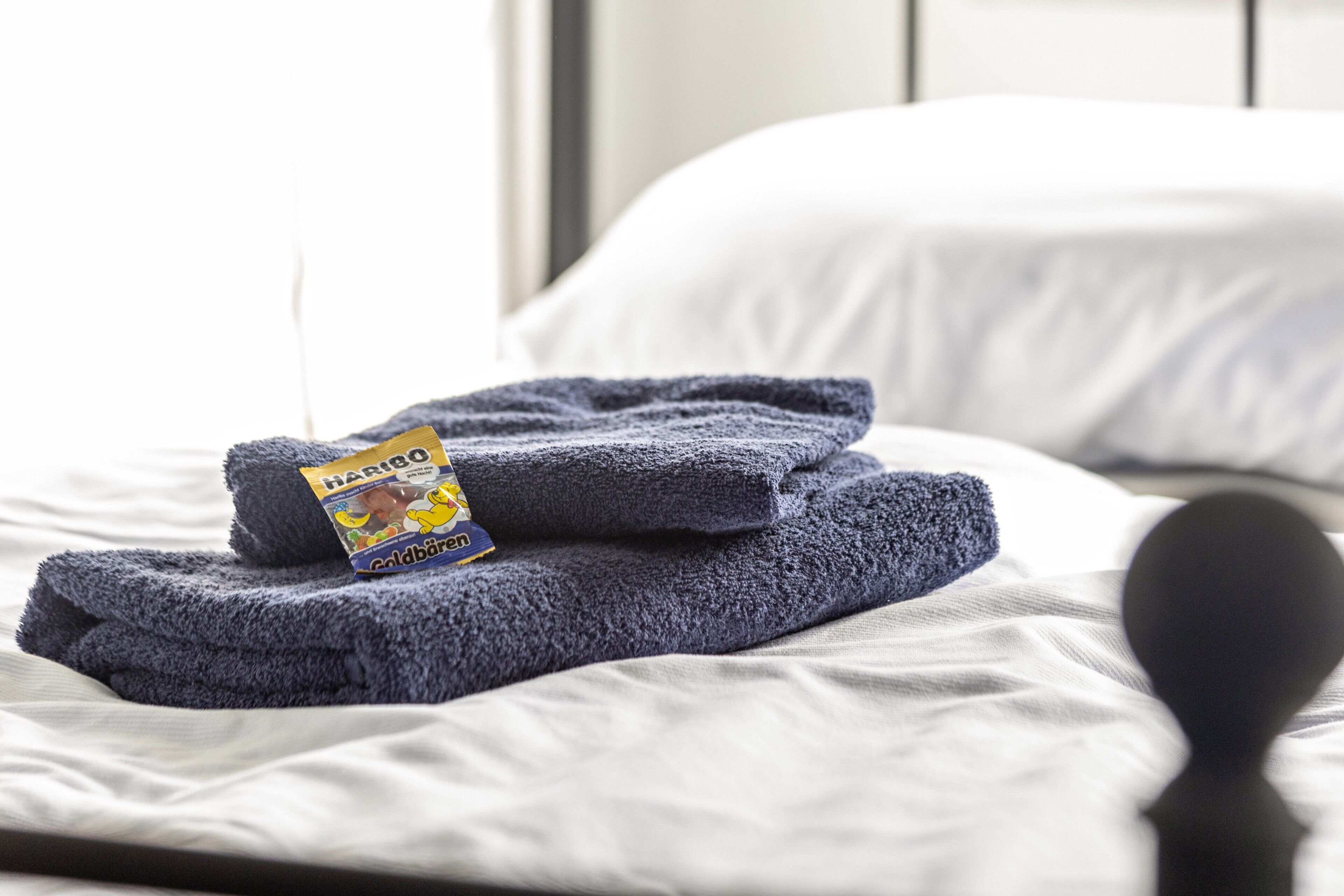 Ein ordentlich bezogenes Bett mit gefalteten Handtüchern und einer Packung Haribo Goldbären.