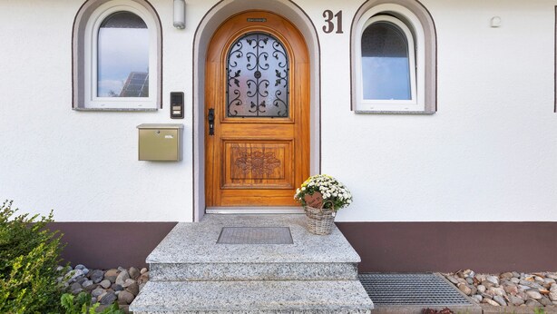 Een huis met een houten deur, het nummer '31' erboven en een bloemenmandje op de treden.