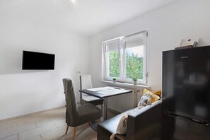 Une pièce de taille modeste comprenant une table à manger, une chaise, un banc, un réfrigérateur noir et un téléviseur fixé au mur.