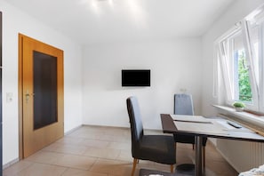 Una habitación con puerta de madera, un televisor de pantalla plana montado en la pared, una mesa de comedor con sillas y una ventana con vistas a zonas verdes.