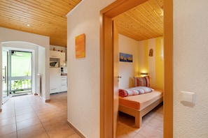 Una habitación con cama, techo de madera, zona de cocina y puerta que da a un espacio exterior.