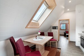 Un coin repas avec un plafond en pente, une table avec des chaises et une vue à travers un puits de lumière.