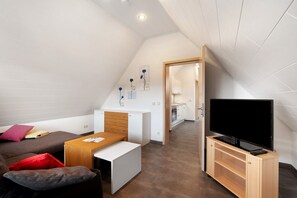 Une chambre moderne de style loft, dotée d’un lit en mezzanine, d’une petite kitchenette, d’un téléviseur posé sur un meuble en bois et d’un coin repas.