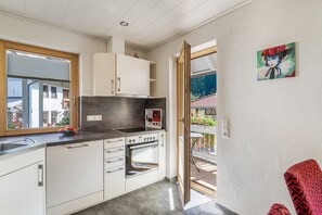 Cocina moderna con armarios blancos, horno empotrado y ventana con vistas a un jardín.