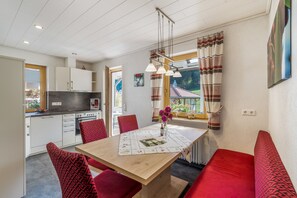 A modern kitchen with white cabinets, a dining table with a floral tablecloth, and red patterned chairs.