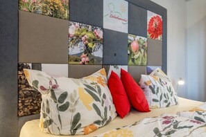 Una cama con almohadas estampadas con motivos florales y un cabecero con arte mural de flores y elementos naturales.