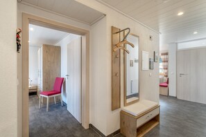 Una habitación de hotel con un banco de madera, un espejo, un perchero de madera y una silla roja.