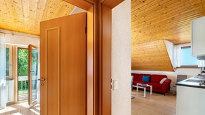 Un intérieur moderne avec un plafond en bois, un canapé rouge, un coin cuisine et une porte-fenêtre coulissante donnant sur un espace extérieur.