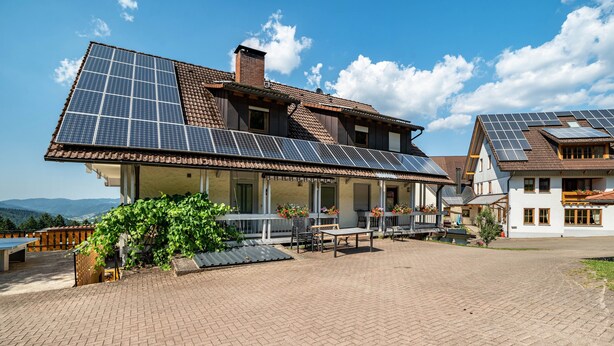 Une maison dotée de panneaux solaires, d’une terrasse dallée et offrant une vue sur les montagnes.