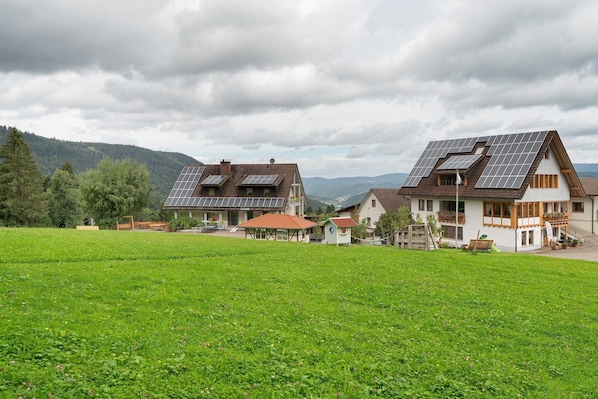 A rural house with solar panels, a garden, and a mountainous backdrop.