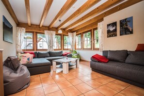 Un salon chaleureux avec des poutres en bois, un canapé, une table basse et de grandes fenêtres.