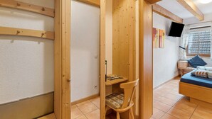 A bedroom with a wooden bed, a desk, a chair, a TV, and a window with a view.