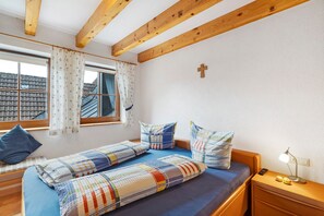 Un dormitorio con dos camas, una ventana con cortinas, techo de madera y una cruz en la pared.
