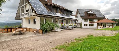 Una casa a due piani con tetto spiovente, pannelli solari, un patio lastricato e una zona verde.