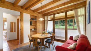 A wooden interior with a dining table, chairs, a red sofa, and a large window with curtains.