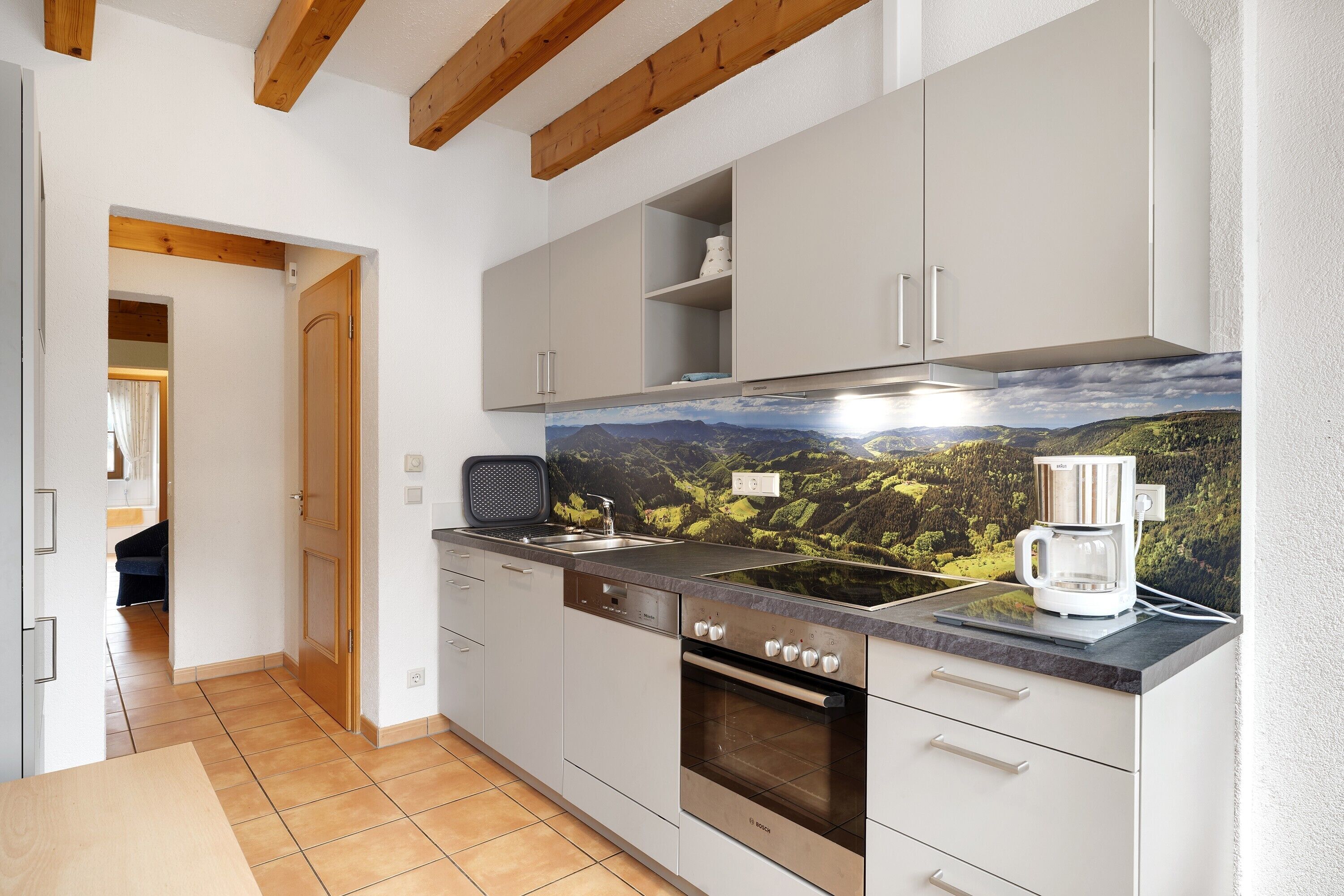 A modern kitchen with a Bosch oven, a coffee maker, and a scenic mural on the wall.