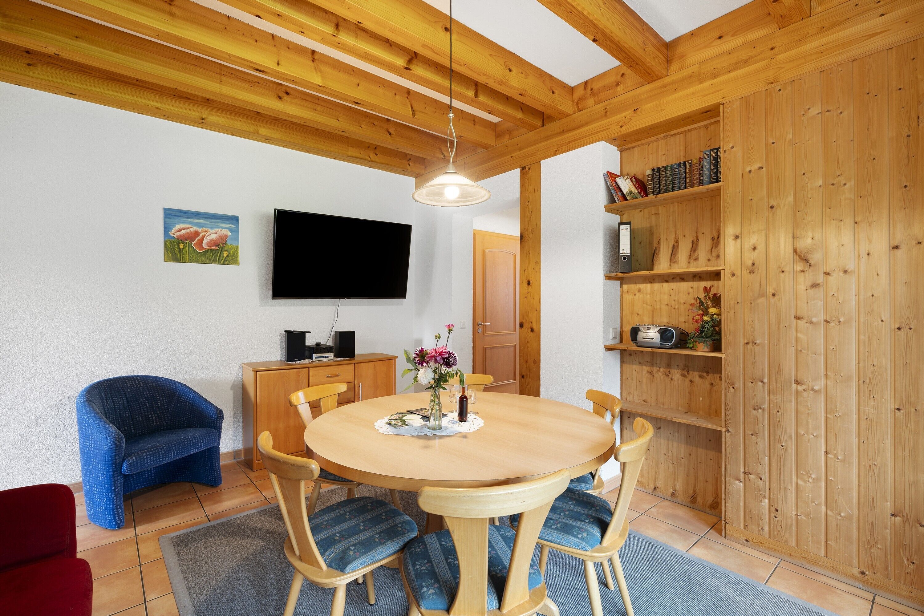 A dining area with a wooden table, chairs, a television, and a bookshelf.