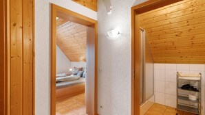 A bedroom with a sloped ceiling, wooden walls, a bed, and a bathroom with a shelf. - Löcherhansenhof: Room 'Double Room 2' with Mountain View, Shared Terrace and Wi-Fi (Bad Peterstal-Griesbach)