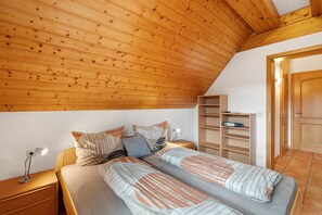 A bedroom with a sloped ceiling, a bed with striped bedding, a bedside table with a lamp, and a built-in shelving unit. - Löcherhansenhof: Room 'Double Room 2' with Mountain View, Shared Terrace and Wi-Fi (Bad Peterstal-Griesbach)
