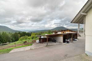 A building with a covered garage, a paved driveway, and a fenced area with trees and hills in the background. - Löcherhansenhof: Room 'Double Room 2' with Mountain View, Shared Terrace and Wi-Fi (Bad Peterstal-Griesbach)