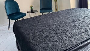 Une chambre d’hôtel moderne avec un grand lit, deux chaises bleues, une petite table avec une plante et un tableau encadré au mur.