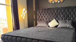 Une chambre avec une tête de lit capitonnée, un grand lit, un tapis noir et un climatiseur fixé au mur.