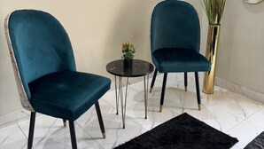 Une pièce avec deux fauteuils de couleur turquoise, une petite table ronde ornée d’une plante, un tapis noir et un tableau représentant une mosquée accroché au mur.