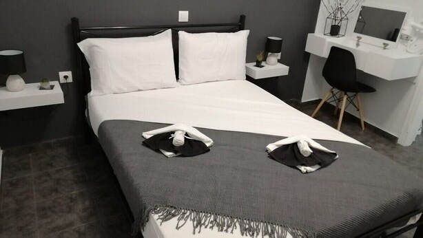 A neatly made bed with white linens and a gray throw blanket, a bedside table with a lamp, and a desk with a chair and a mirror. - Sabbia Calda  apt 8 by Comfortbnb (Perissa)