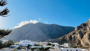 A coastal town with white buildings, a mountain in the background, and dry vegetation in the foreground. - Sabbia Calda  apt 8 by Comfortbnb (Perissa)