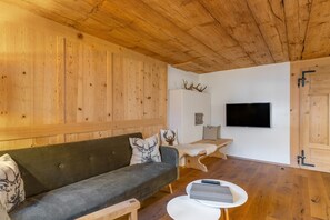 A wooden interior with a sofa, a small table, a TV, and antlers on the wall.