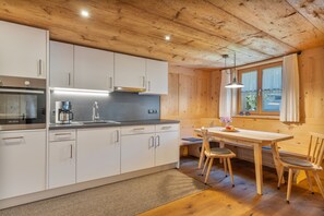 A modern kitchen with white cabinets, a stainless steel range hood, and a wooden dining table with chairs.