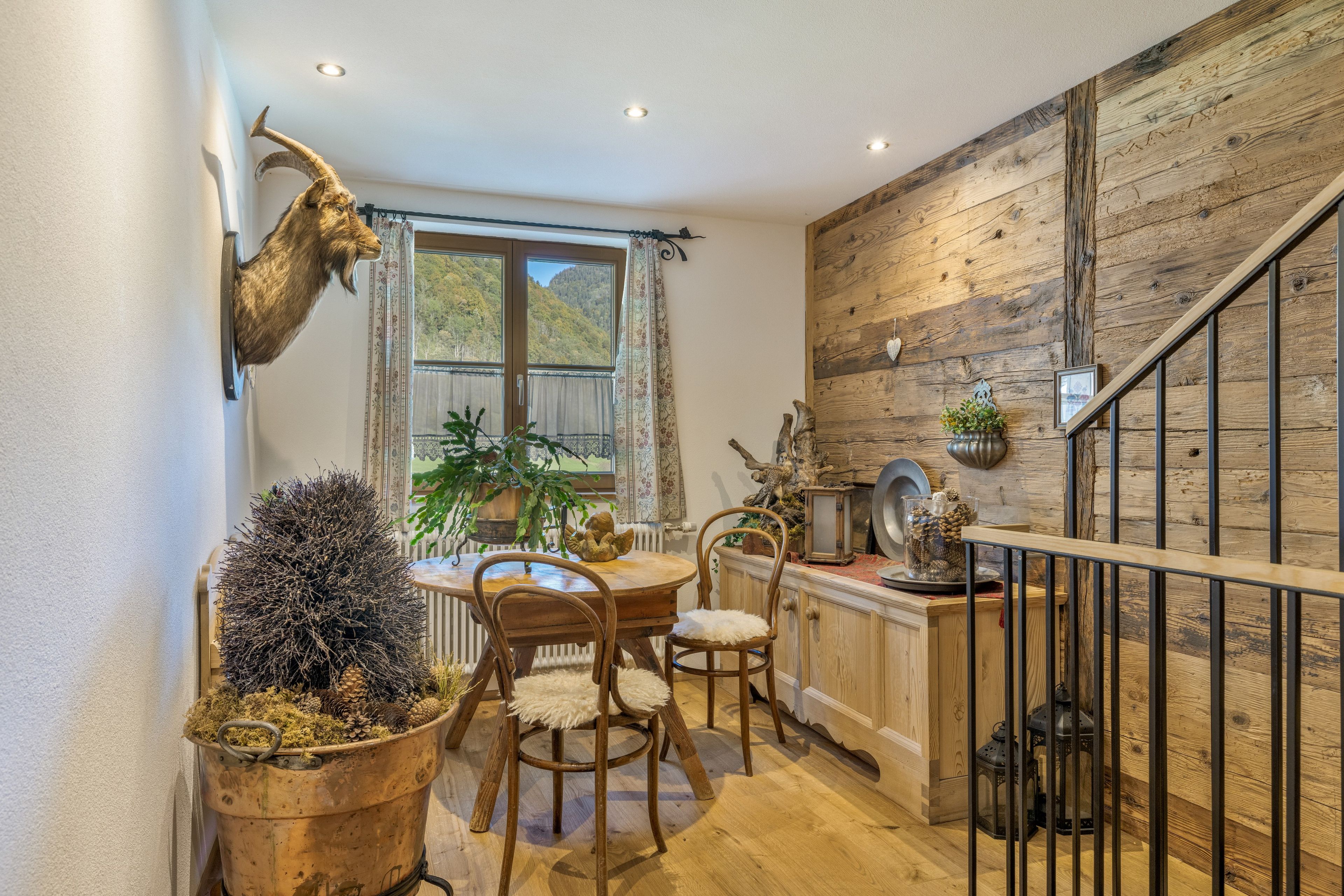 Ein rustikales Interieur mit einer Holztreppe, einem Essbereich mit Holzsesseln und einem aufgehängten Tierkopf.