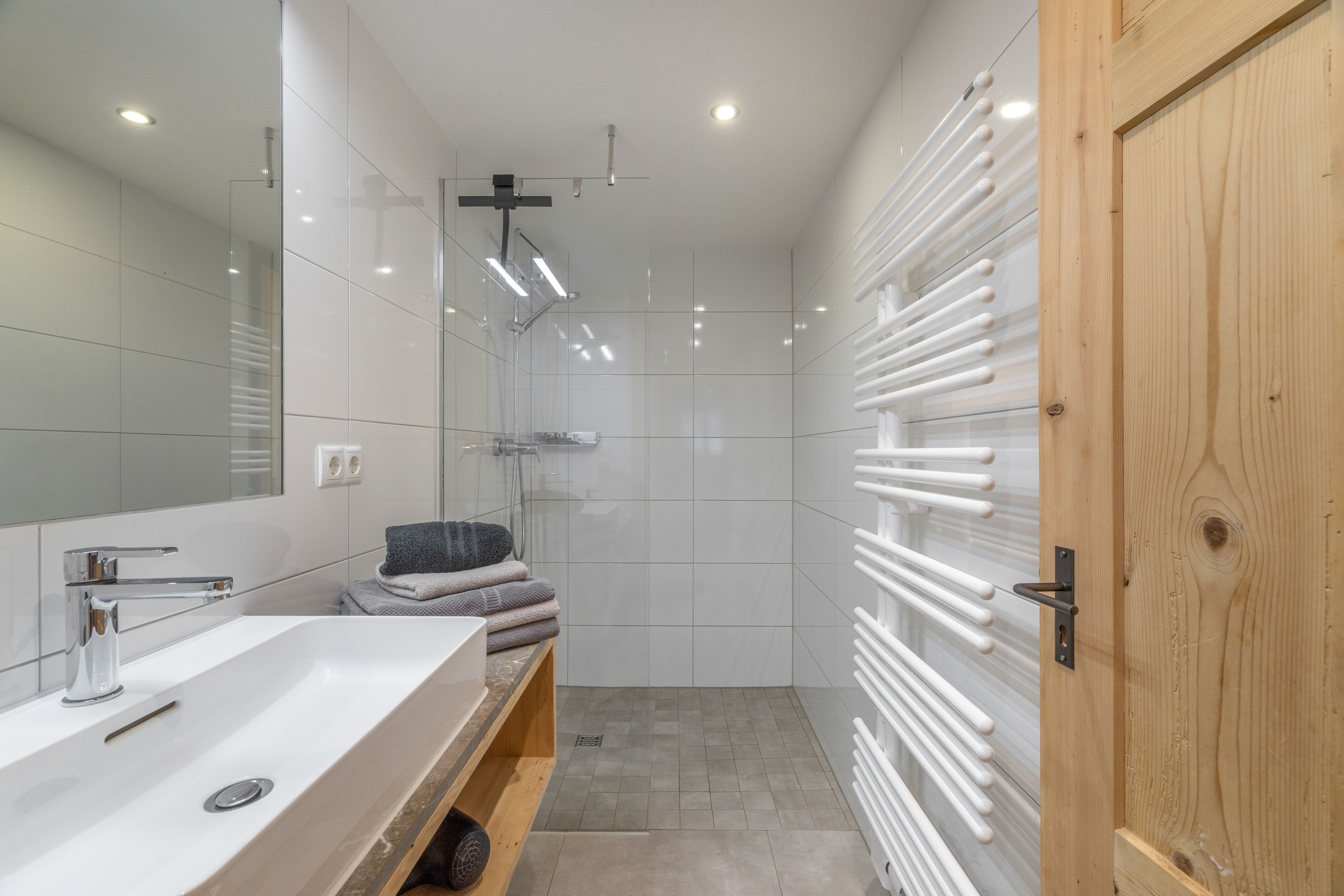 Ein modernes Badezimmer mit Waschbecken, Spiegel und Dusche, alles in Weiß.