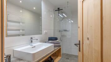 Ein modernes Badezimmer mit großem Spiegel, Waschbecken in Weiß, Dusche und Holztür.