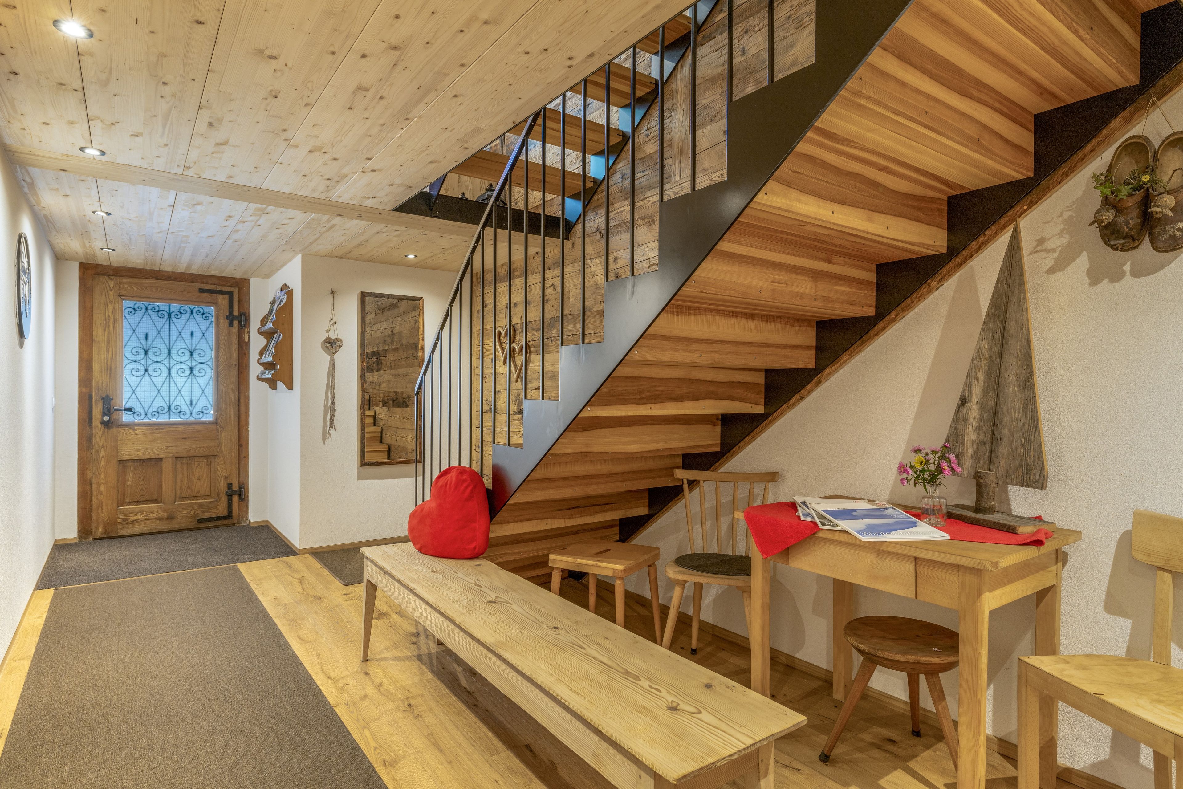 Eine Holztreppe mit modernem Design, eine Bank, ein Tisch mit Blumenvase und eine Holztür.