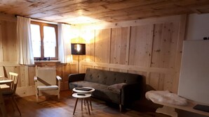 Een kamer met houten lambrisering, een bank, twee stoelen, een kleine tafel en een lamp.