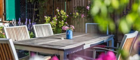 A wooden table with chairs, a blue vase with flowers, and a wooden fence in the background.