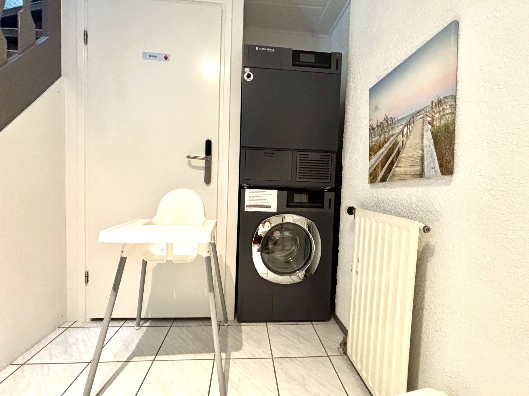 Une petite buanderie comprenant un lave-linge, un étendoir et une petite chaise blanche.
