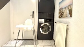 Une petite buanderie comprenant un lave-linge, un étendoir et une petite chaise blanche.